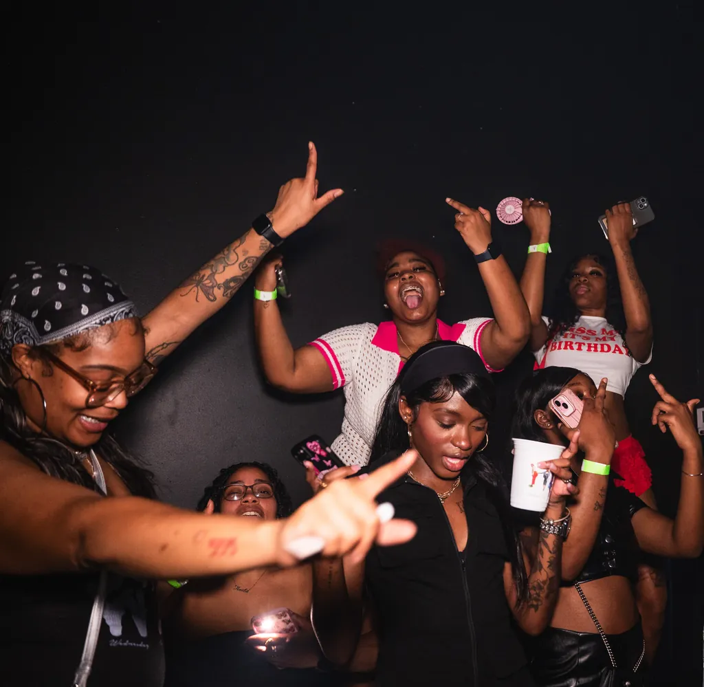 A birthday group with hands up and phones out, lit by the flash