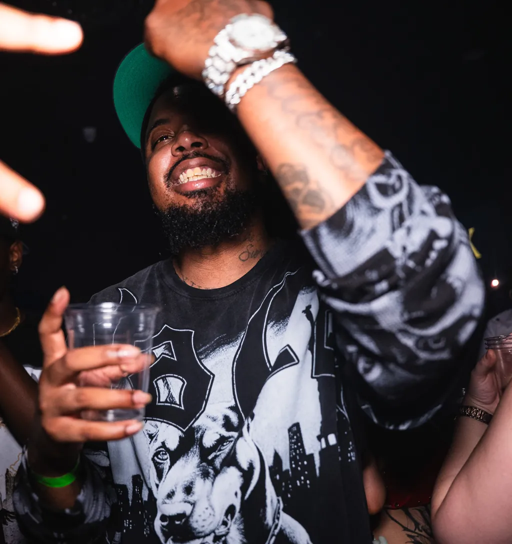 A man laughing with a cup in his hand and his arm up in the crowd