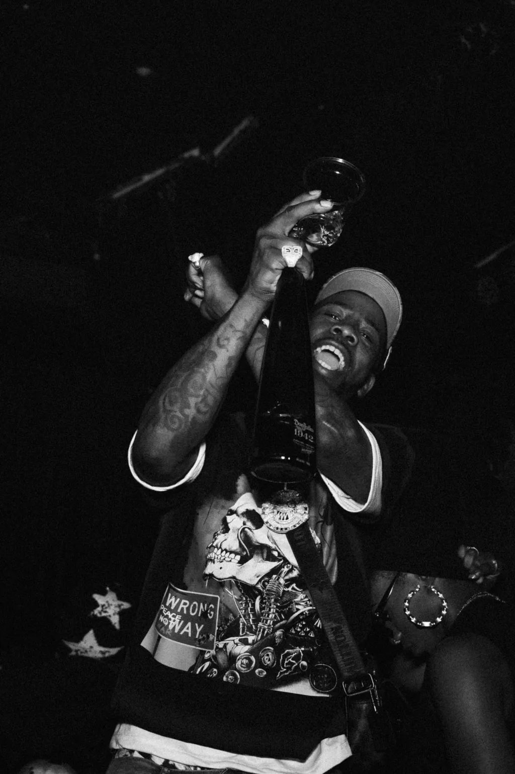 Black and white: a man in a graphic tee lifts a bottle over his head in a dark club