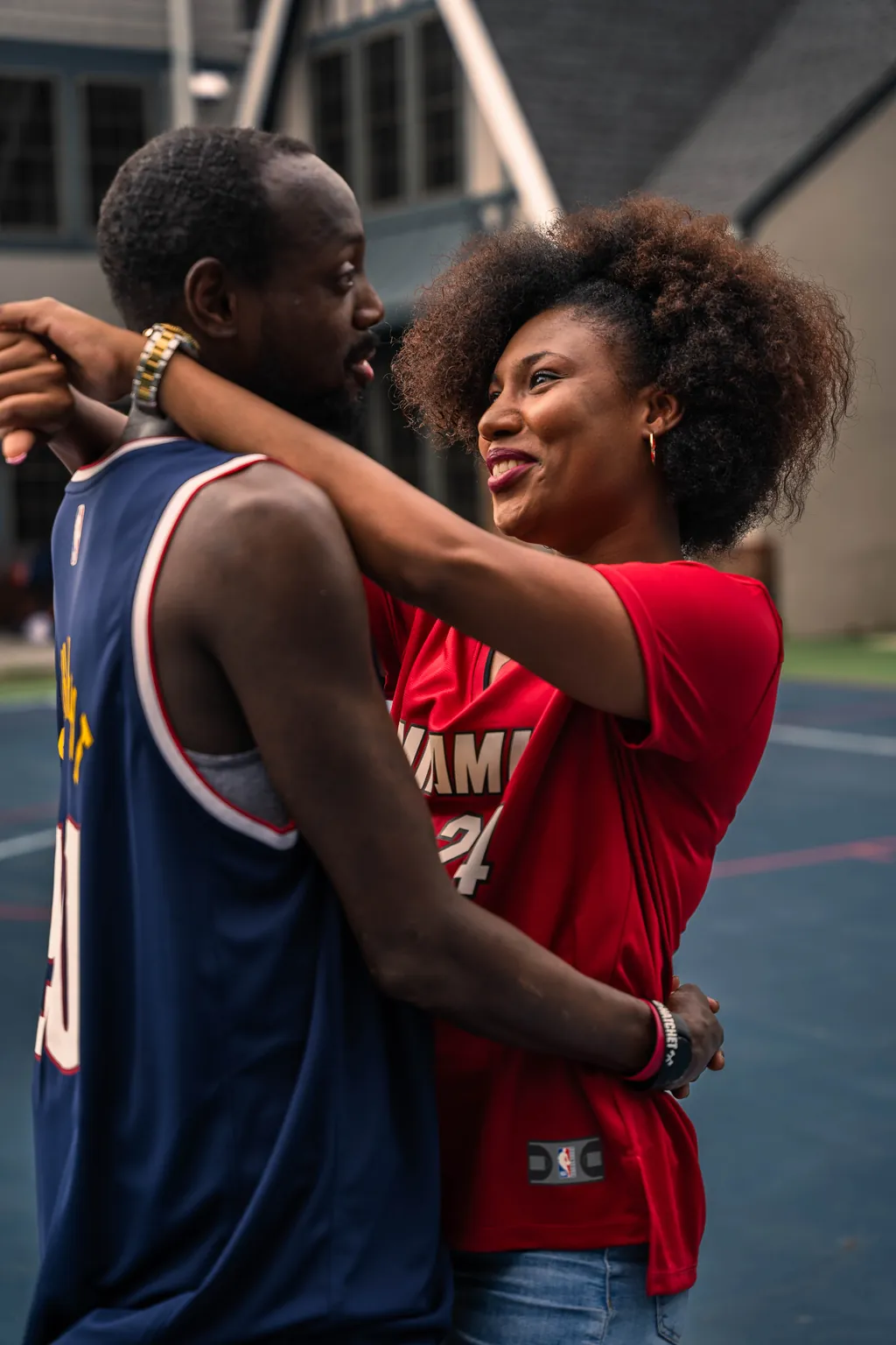 An engaged couple in basketball jerseys holding each other on an outdoor court